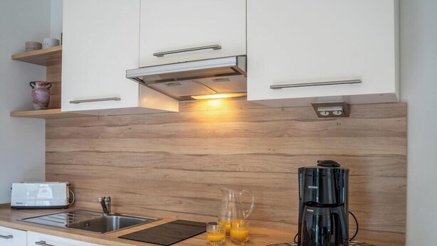 Una cucina moderna con mobili bianchi, una schiena di legno, una macchina per il caffè e un tostapane.