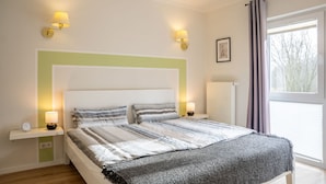 Una camera da letto con un letto, abat-jour, una sveglia, un termosifone e una finestra con tende.