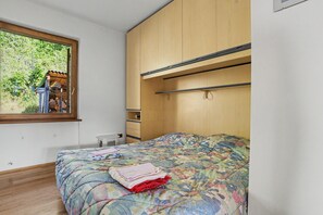 A bedroom with a bed, a window, and a wooden wardrobe.