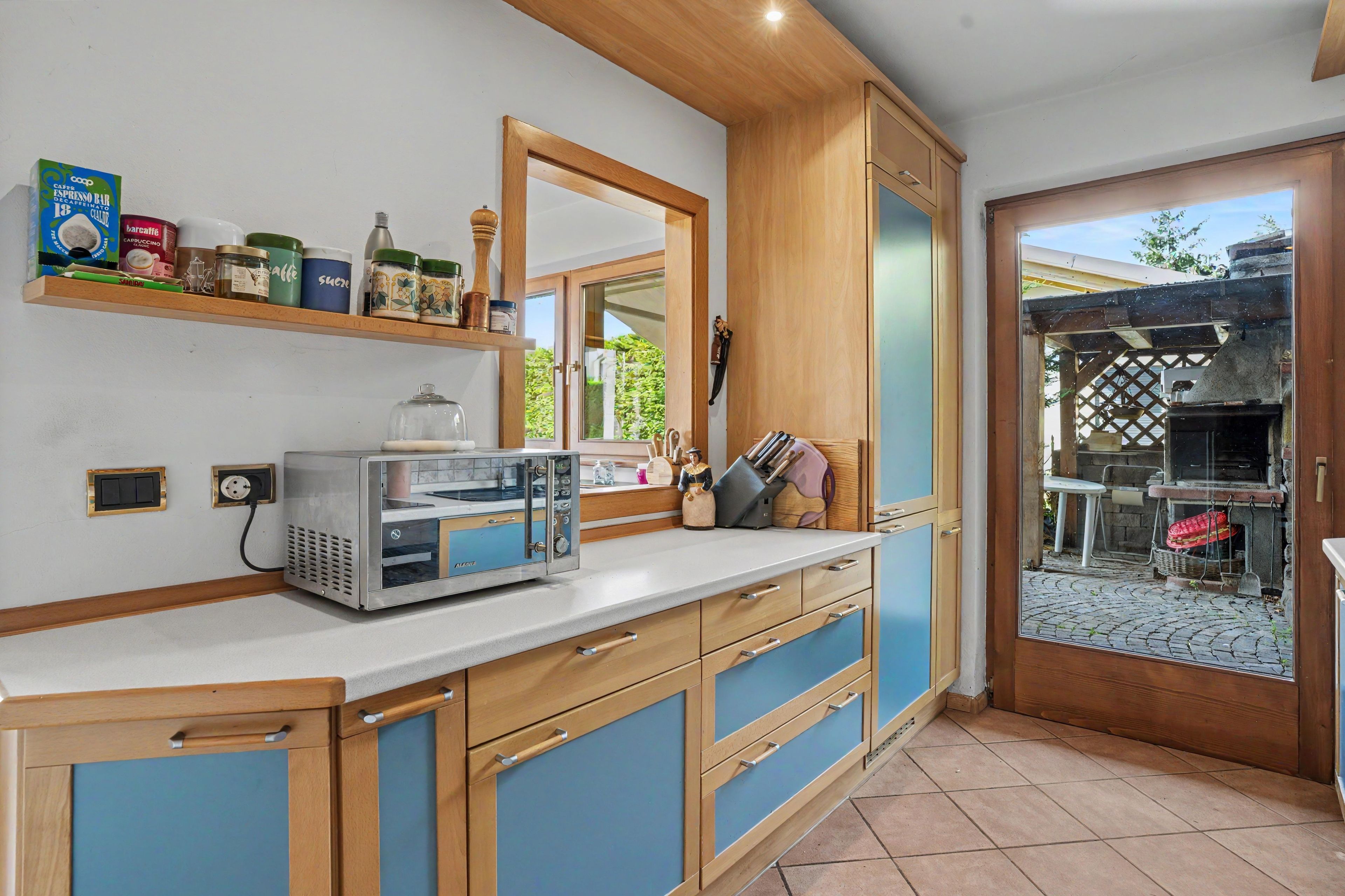 Eine Küche mit integriertem Espressomaschine, Holzschränken und einem Fenster mit Blick auf einen Garten.