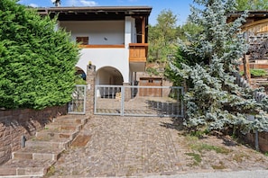 A stone staircase leading to a wooden gate with a metal fence, surrounded by greenery and a building with a sloped roof.