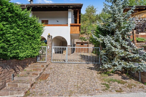 A stone staircase leading to a wooden gate with a metal fence, surrounded by greenery and a building with a sloped roof.