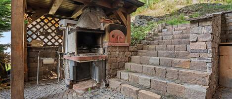 An outdoor brick oven with a chimney, a stone staircase, and a wooden pergola structure.