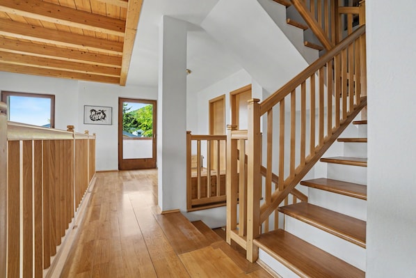 A wooden staircase with a handrail, leading to a landing with a door and a window.