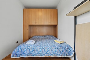 A small, single-bed room with a wooden wardrobe above the bed and a ceiling fan on the right.