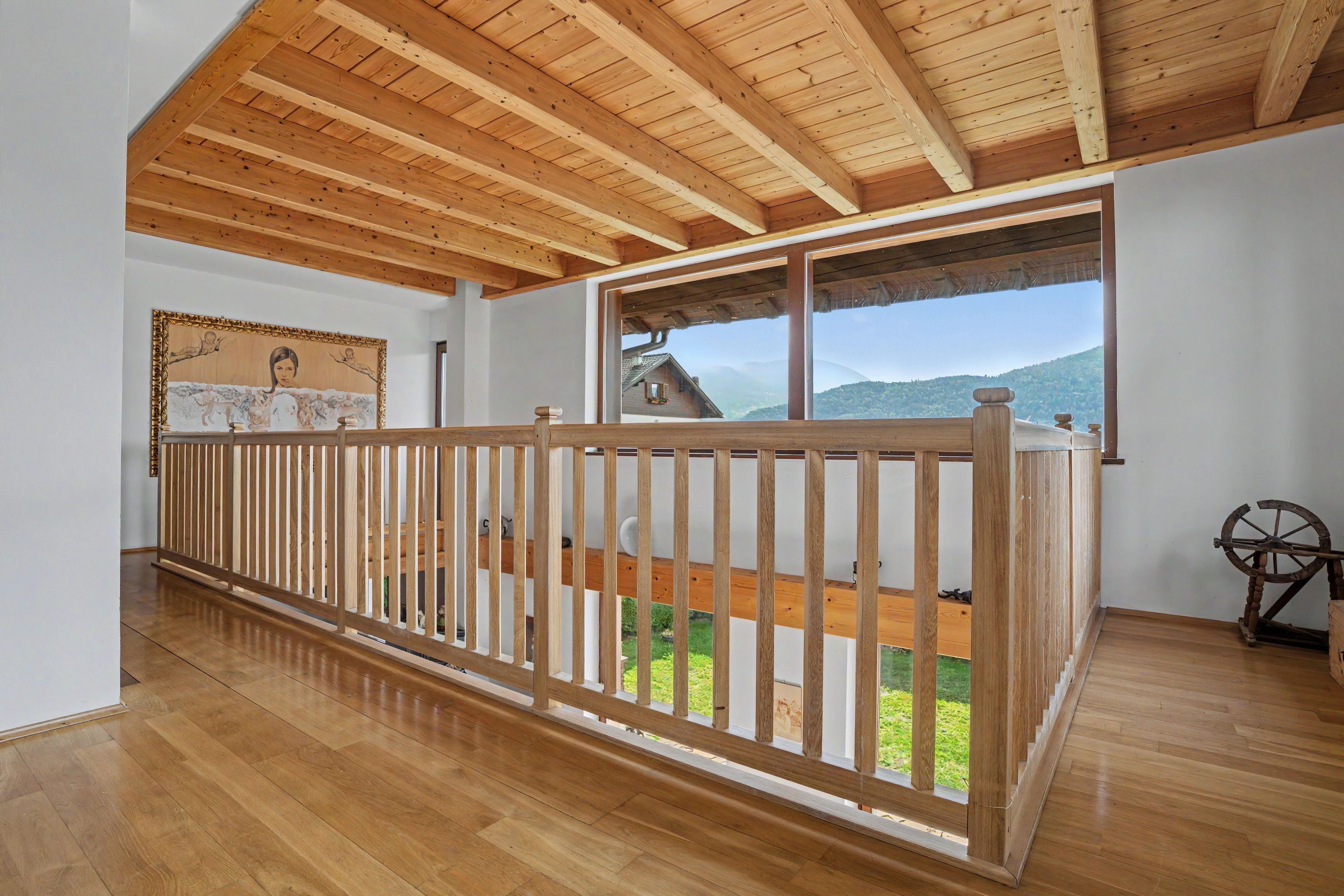 Una habitación amplia con techo de madera, un balcón con barandilla de madera y un gran ventanal con vistas al exterior.