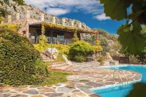 A stone pool with a stone deck leading to a building with a stone facade and a covered patio area.