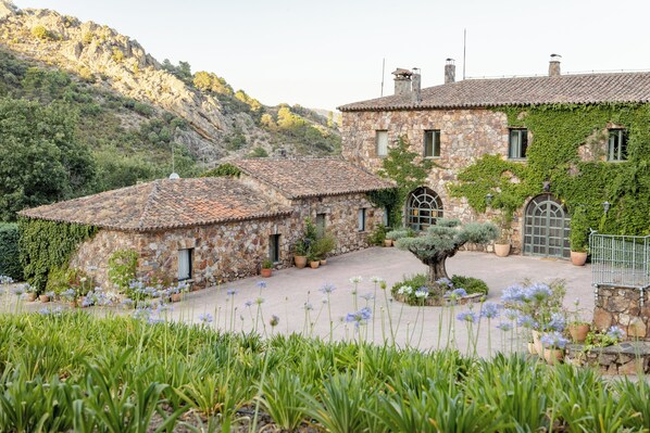 A stone building with a tiled roof, surrounded by a garden with flowers and plants.