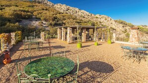 Zona d'estar a l'aire lliure amb taules i cadires, un cobert i vistes a un paisatge de muntanya.