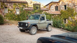 Un vehicle tot terreny Mercedes-Benz estacionat davant d'un edifici de pedra amb parets cobertes d'herba i un teulat de teules.