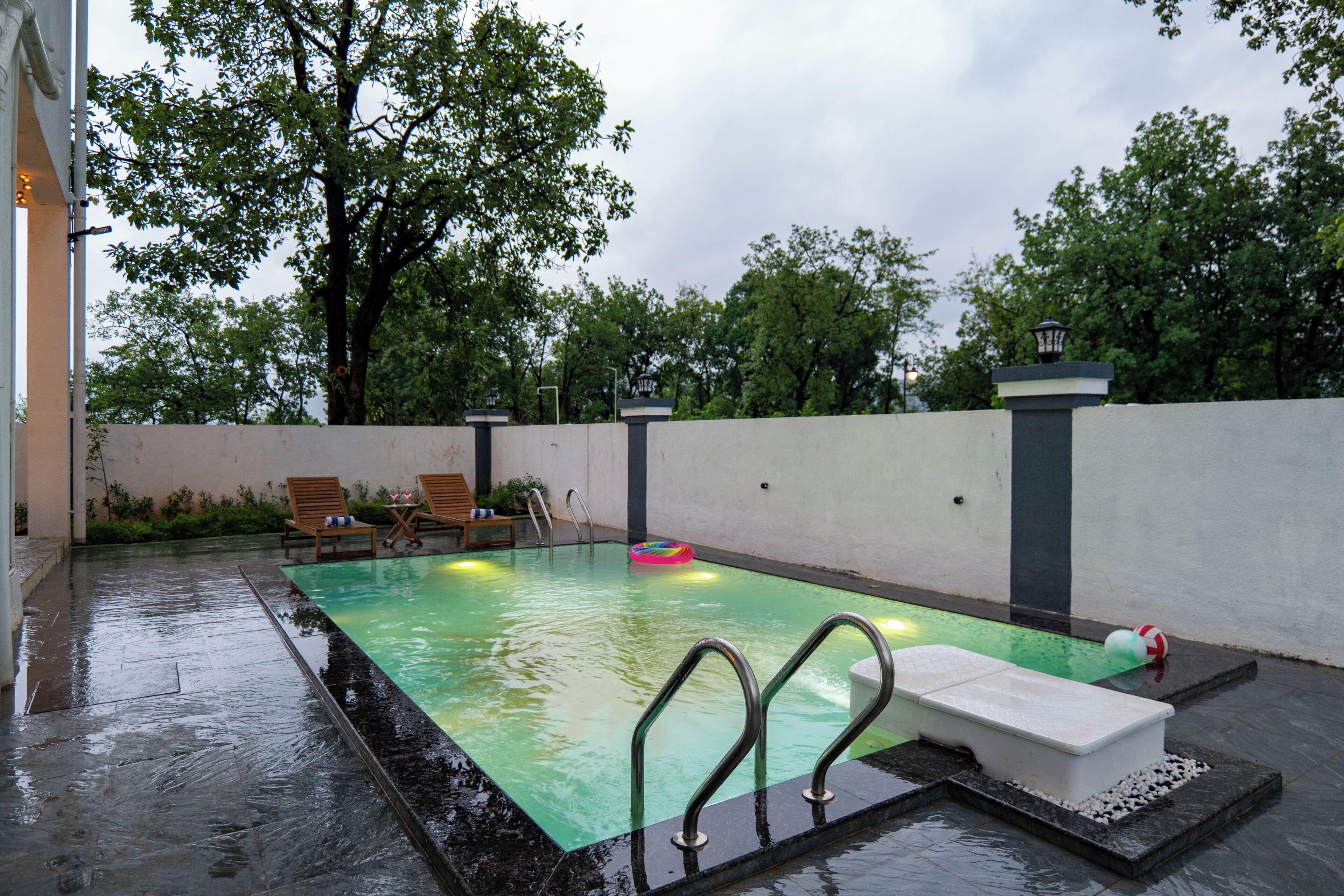 Una piscina con solárium de baldosas, una zona de descanso con sillones y una pared con farol.