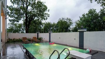 Una piscina con solárium de baldosas, una zona de descanso con sillones y una pared con farol.