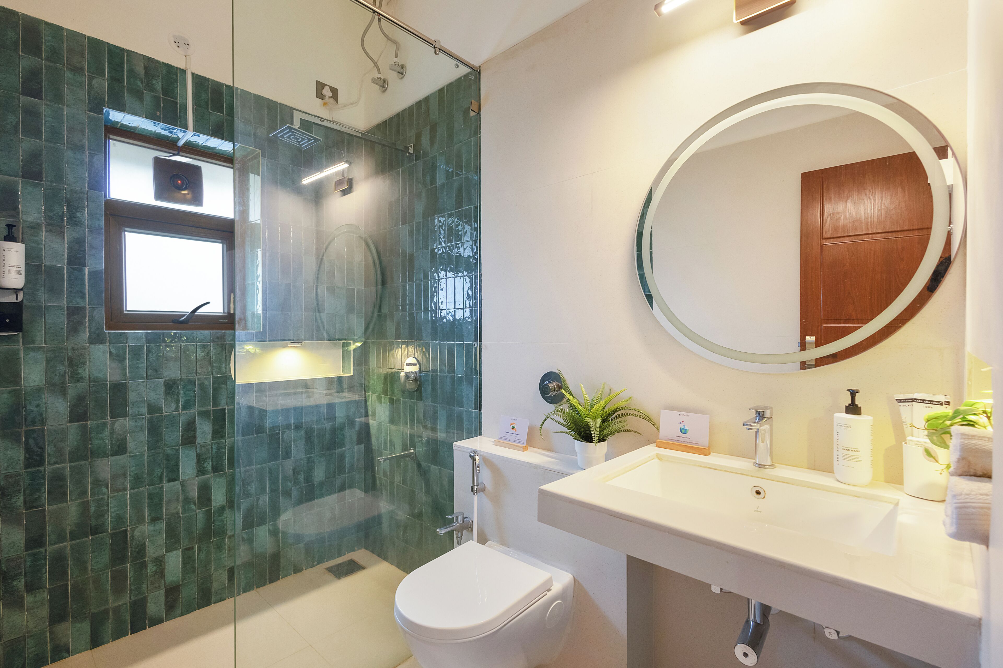 Une salle de bain moderne avec une douche à parois de verre, des toilettes blanches, un lavabo avec un miroir et des articles de toilette.