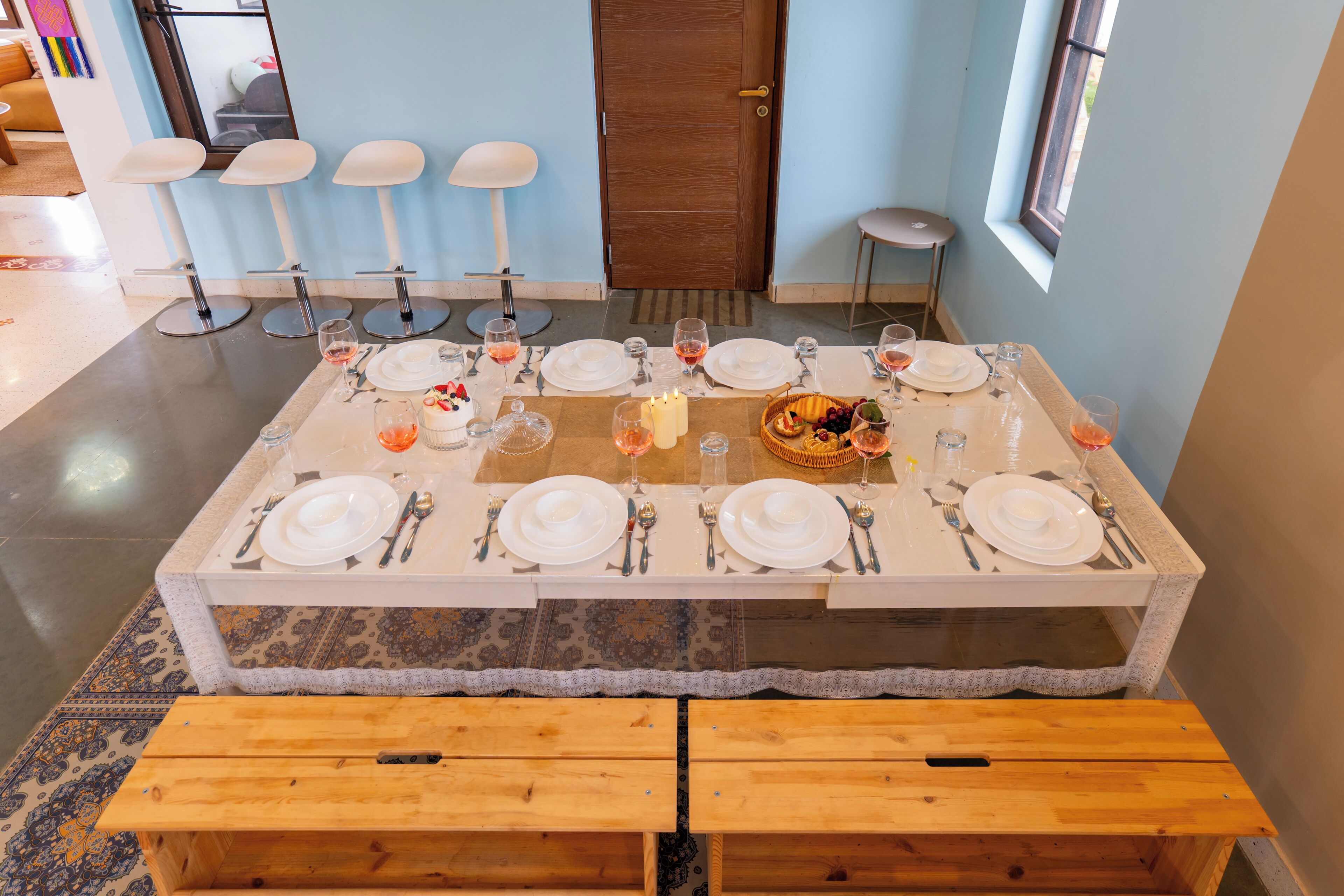 A dining area with a rectangular table set for a meal, benches in front, and a door in the background.