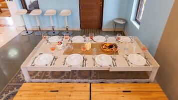 A dining area with a rectangular table set for a meal, benches in front, and a door in the background.