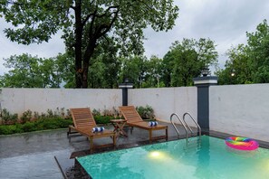 A pool area with two wooden lounge chairs, a small table, and a colorful inflatable ring.