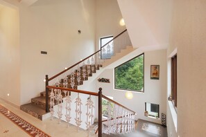 A staircase with ornate white railings and a wooden handrail, leading to a landing with a large window offering a view of greenery.