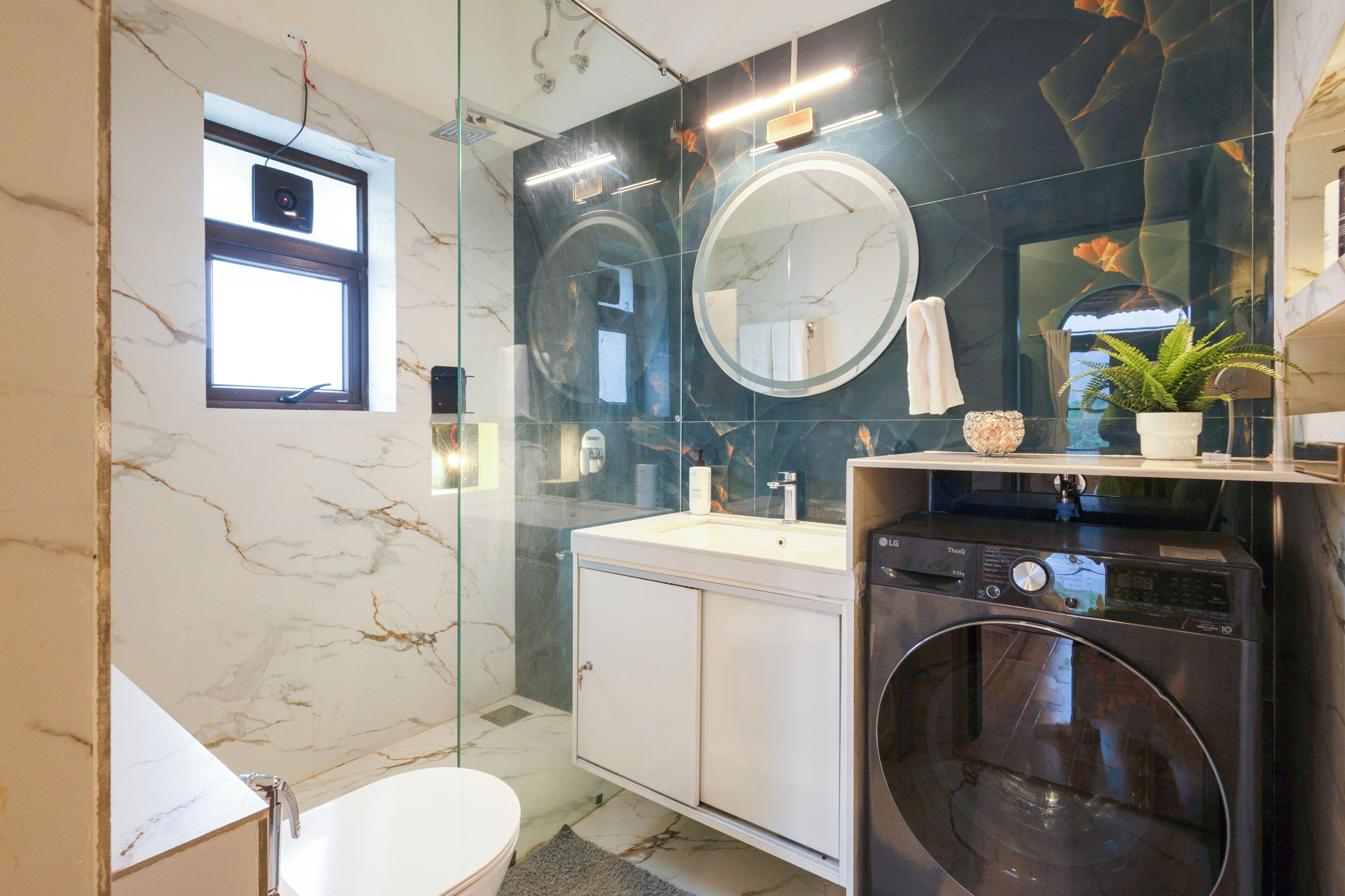 A modern bathroom with a glass shower enclosure, a built-in washing machine, and a large mirror above the sink.
