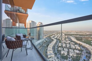 Ein Balkon mit Glasgeländer, einem Tisch, zwei Stühlen und Blick auf eine Stadtlandschaft.