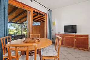 Un coin repas avec une table et des chaises en bois, un panier en osier et un téléviseur posé sur un meuble en bois.