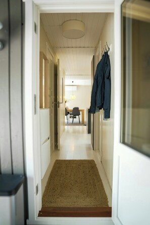 A hallway with a wooden floor, a rug at the entrance, and a coat rack with a jacket. - Nordic retreat with wilderness bath near Marielyst (V)