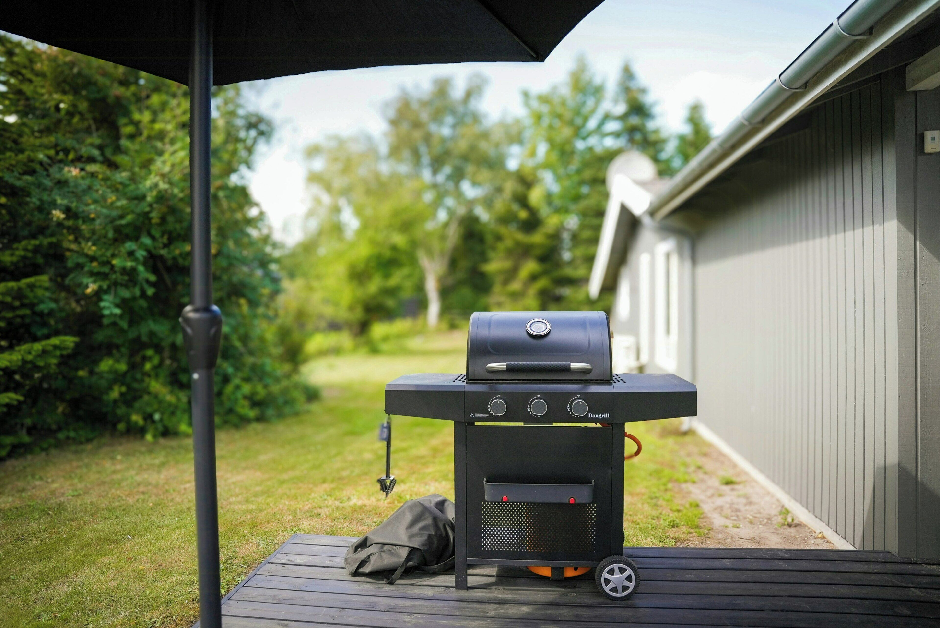 A barbecue grill with controls and a bag on a wooden deck.