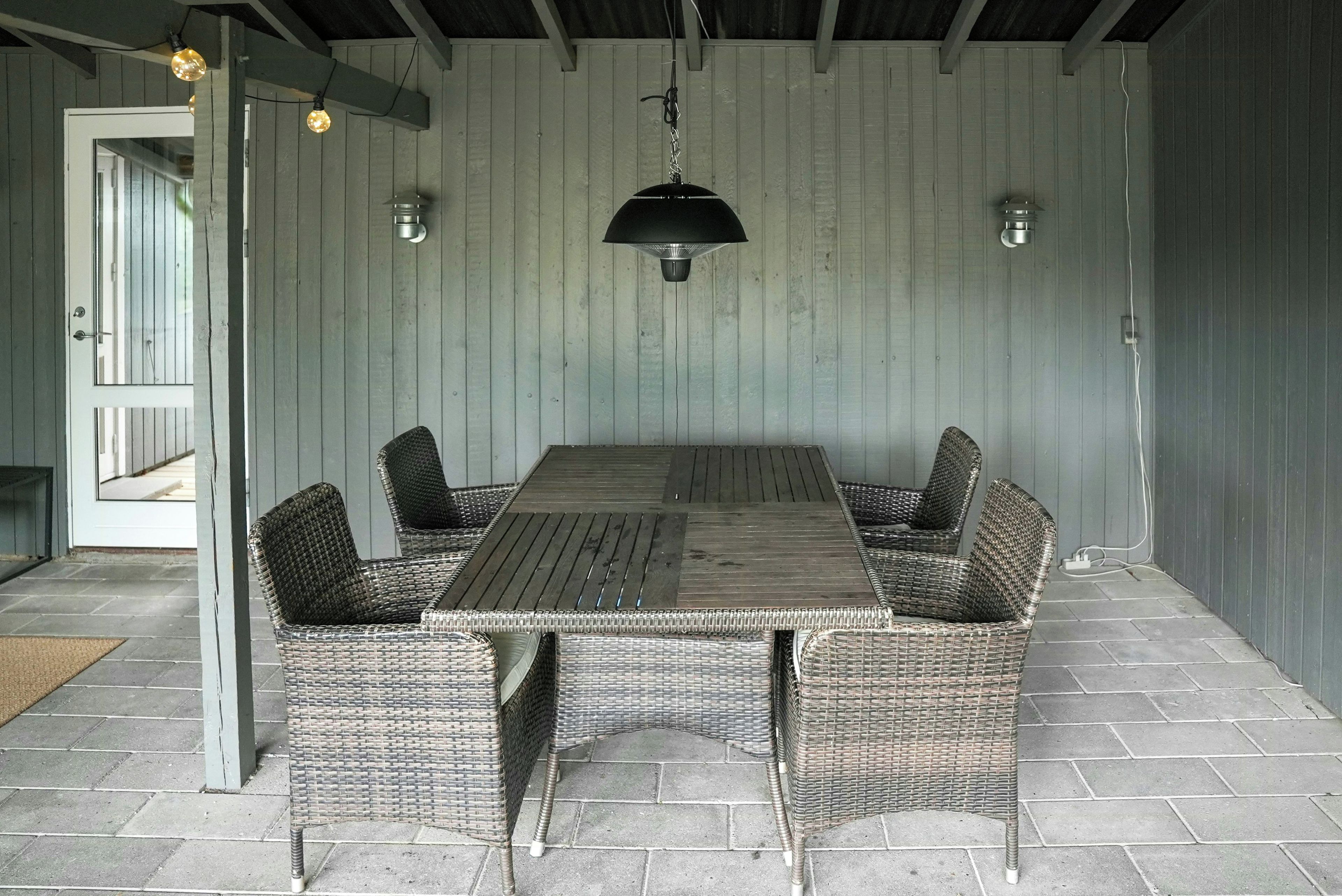 A dining area with a long table and wicker chairs, a hanging light fixture, and a door leading outside.