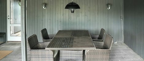 A dining area with a long table and wicker chairs, a hanging light fixture, and a door leading outside.