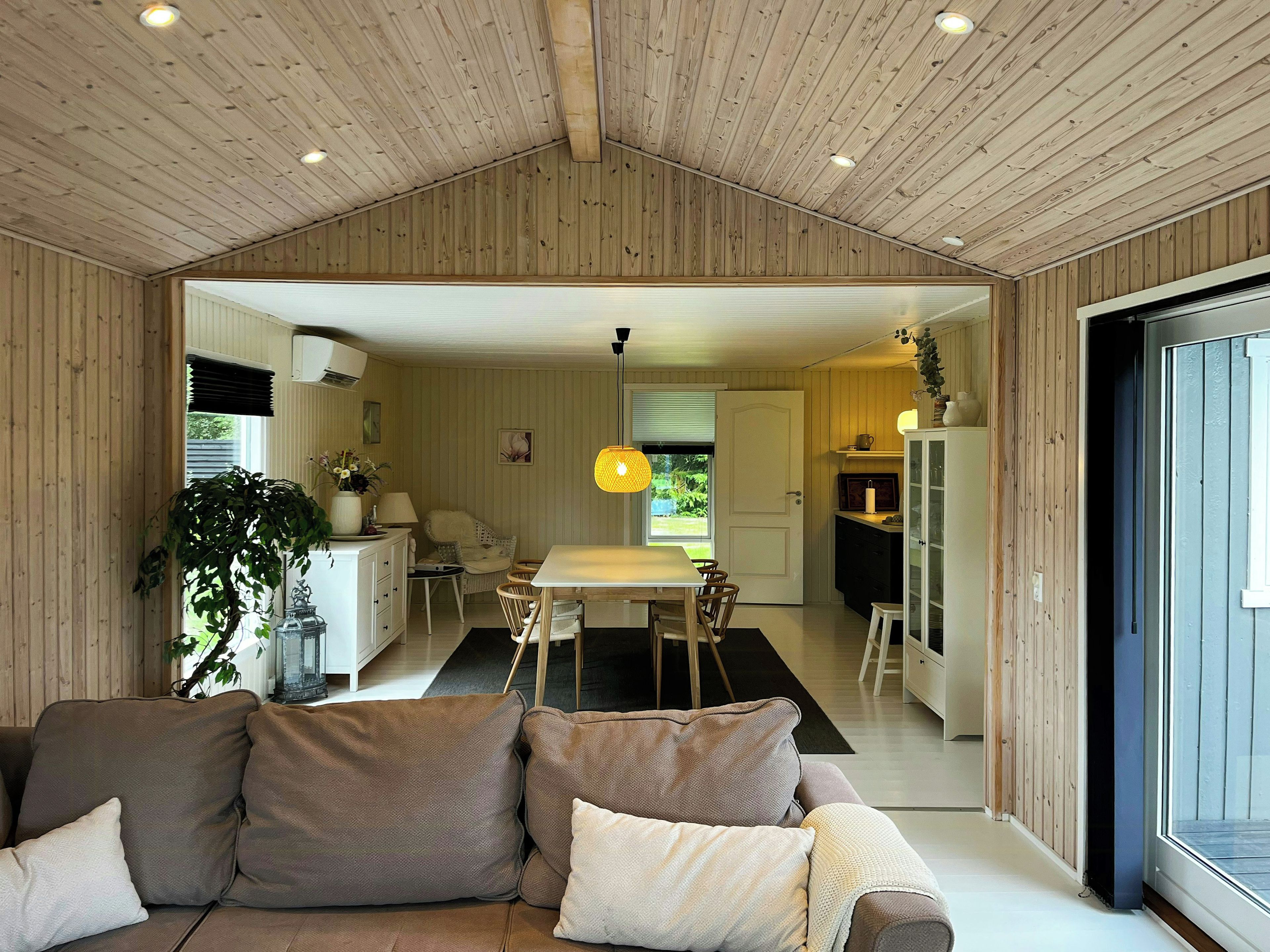 Een modern interieur met een houten plafond, een eethoek met tafel en stoelen, een bank met kussens en een keuken met kasten en een koelkast.