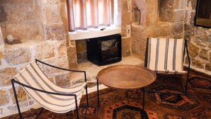 Quarto com paredes de pedra, duas cadeiras, uma mesa redonda e um tapete estampado.