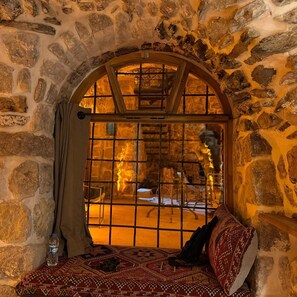 Una habitación de paredes de piedra con un banco, una ventana con barrotes y una botella sobre el banco.