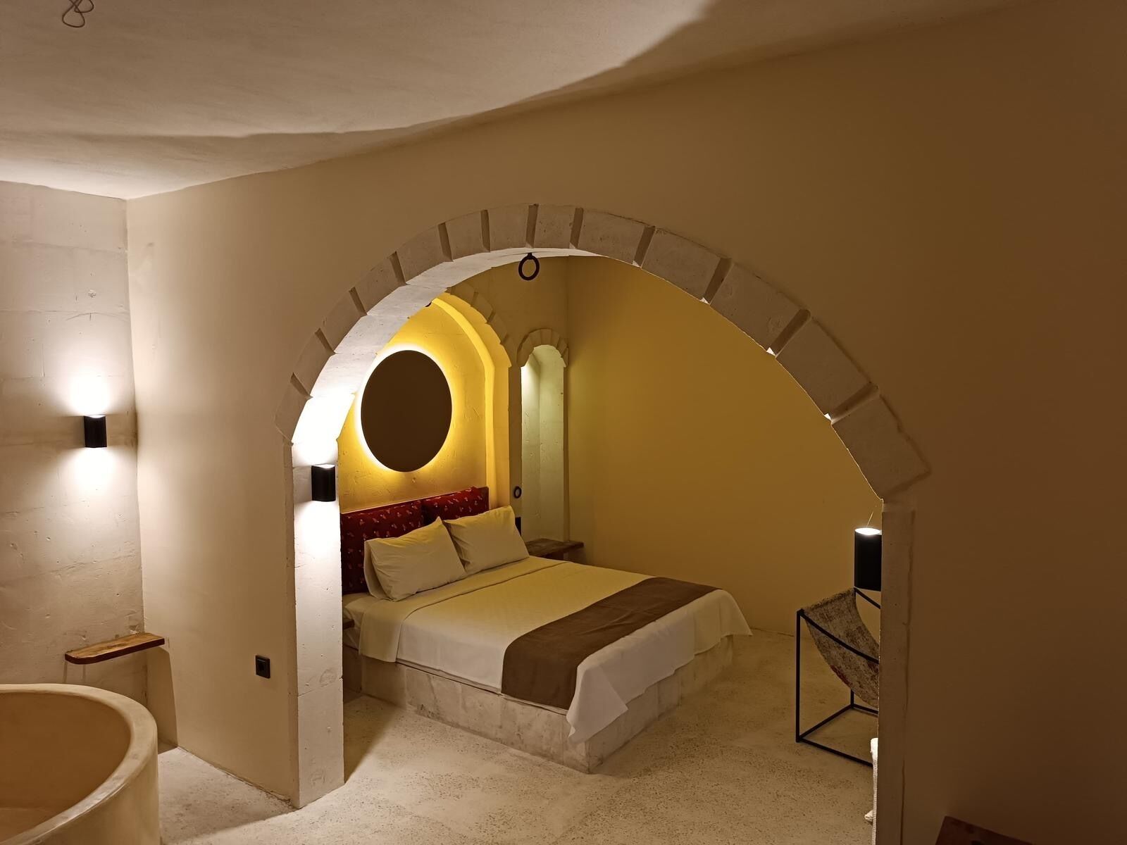 A bedroom with a bed, a circular light fixture, and a small table.