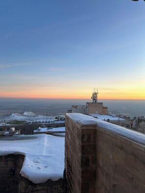 Tejado cubierto de nieve con vista a un horizonte lejano y un atardecer.