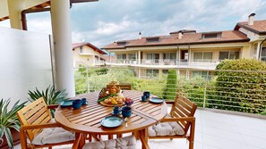 A round wooden table with chairs, a buffet of pastries, and blue cups on a balcony overlooking a residential area with a white railing and greenery. - Sirmio Dream View Suite by Bookinggardalake (Sirmione)