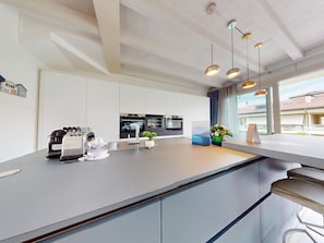 A modern kitchen with built-in appliances, a large window, and a view of the outside. - Sirmio Dream View Suite by Bookinggardalake (Sirmione)