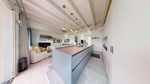A modern kitchen with a central island, a dining area with a sofa, and a TV. - Sirmio Dream View Suite by Bookinggardalake (Sirmione)