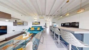 A modern living room with a sofa, coffee table, and a TV. There is a kitchen area with a bar and seating. - Sirmio Dream View Suite by Bookinggardalake (Sirmione)