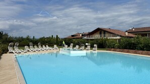 A swimming pool with lounge chairs, a clear sky, and residential buildings in the background. - Sirmio Dream View Suite by Bookinggardalake (Sirmione)
