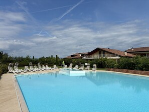 A swimming pool with lounge chairs, a clear sky, and residential buildings in the background. - Sirmio Dream View Suite by Bookinggardalake (Sirmione)