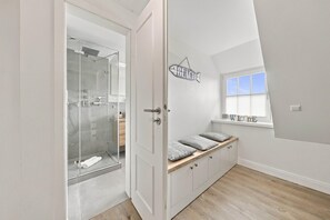 A modern bathroom with a glass shower enclosure, a vanity with a sink, and a window with a view of the sky. - Rundblick Building, Apartment 8 (Sylt)