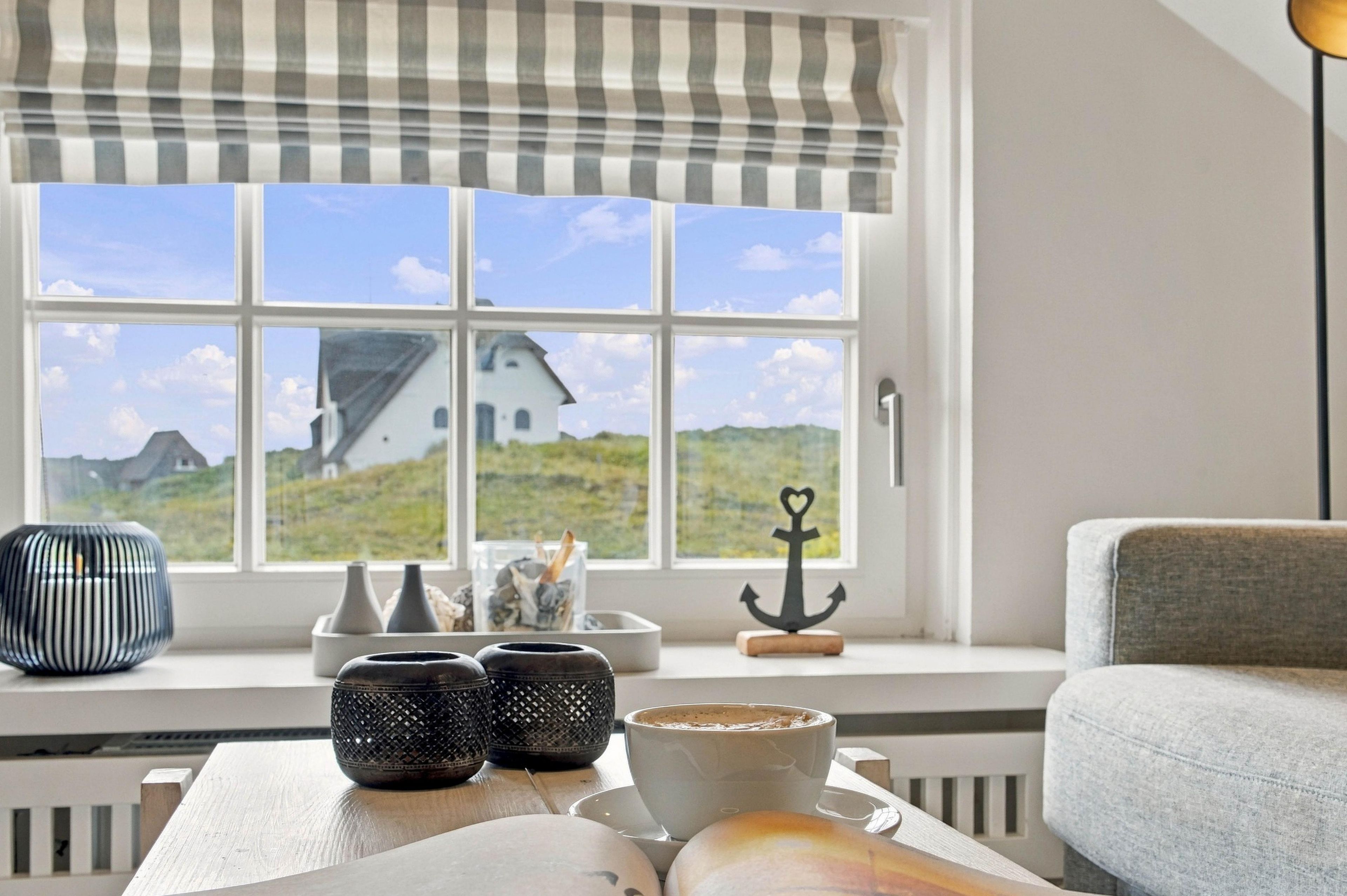 A room with a large window, a view of a house, and a table with decorative items.