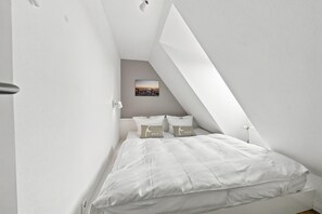 Een slaapkamer met een schuine kap, een bed met wit beddengoed en één afbeelding aan de muur.