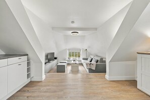 Een moderne loft slaapkamer met schuine plafonds, een ingebouwde televisie, een raam met uitzicht en een knus zitgedeelte.