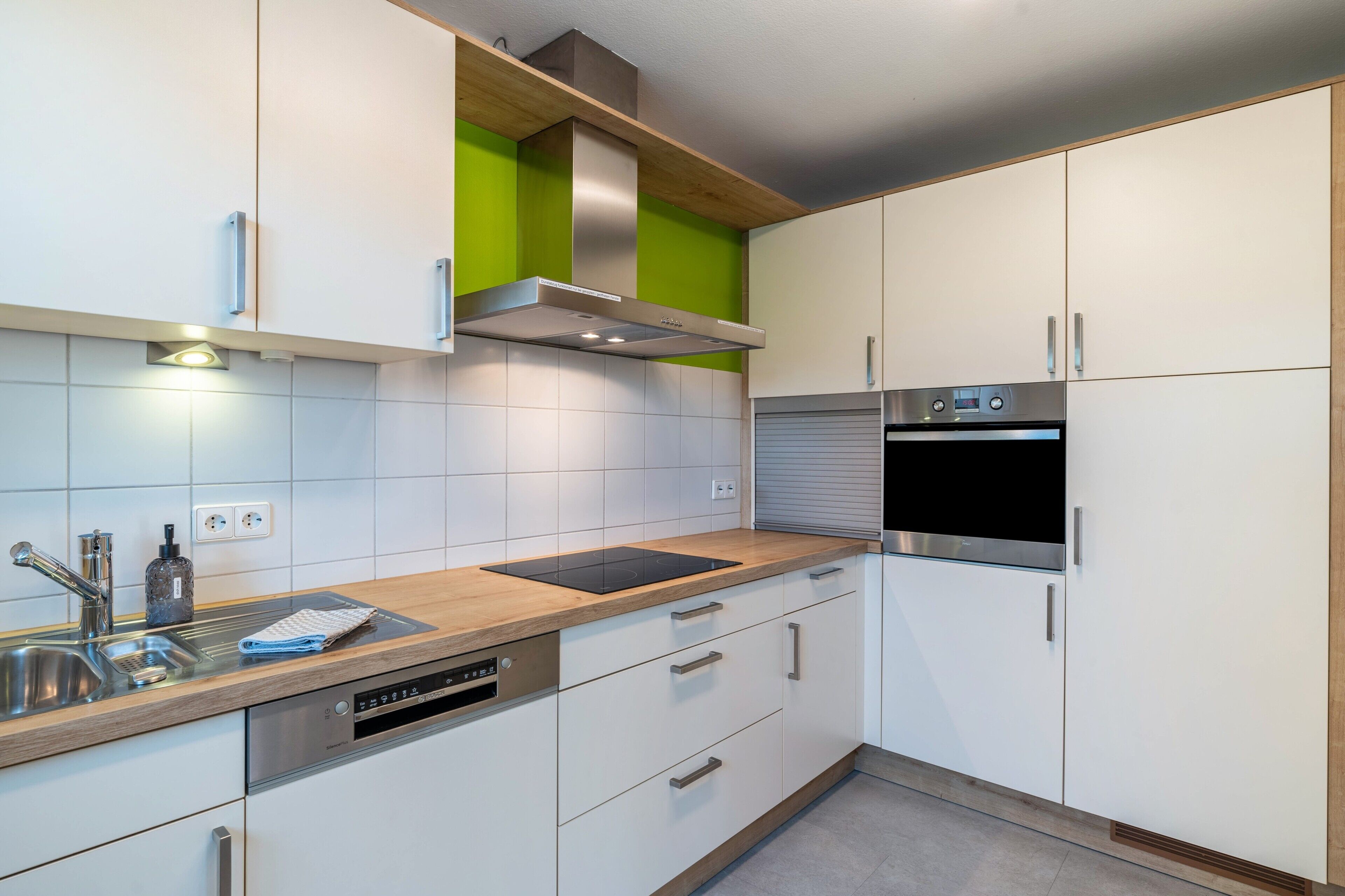 Eine moderne Küche mit weißen Schränken, einer Edelstahl-Dunstabzugshaube, einem Backofen und einem Geschirrspüler.