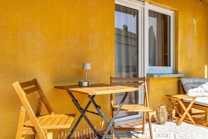 Un pequeño espacio al aire libre con mesa y sillas, una lámpara y una ventana con vistas a edificios.