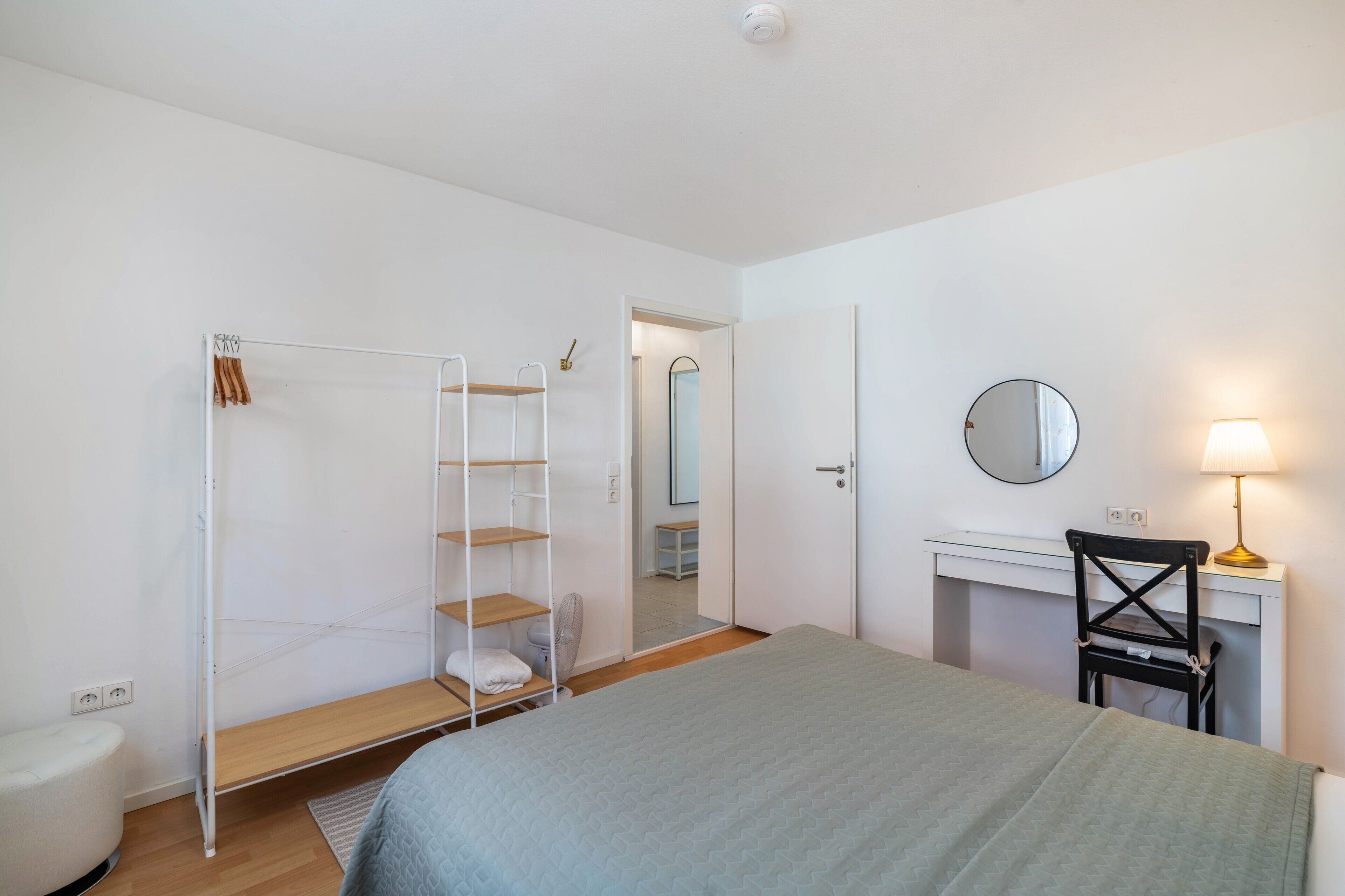 Ein Schlafzimmer mit Bett, Schreibtisch, Stuhl, Kleiderschrank und Spiegel.