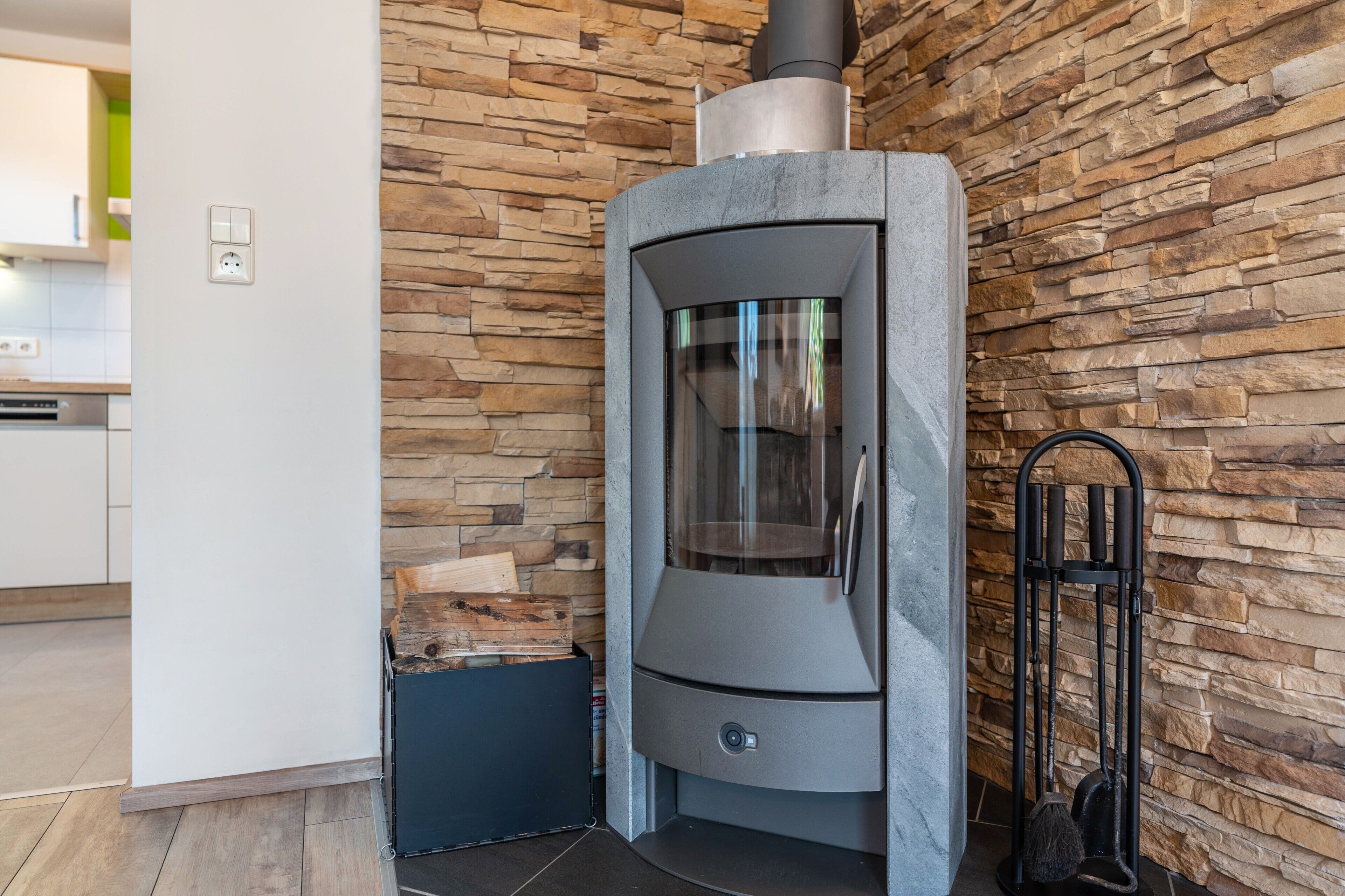 A modern kitchen with a stone wall, a built-in wood stove, and a black metal gate.