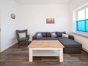 A modern living room with a sectional sofa, a wooden coffee table, a grey armchair, and a wall clock. - Modern Ostdeich vacation rental in Büsum with a terrace for the whole family (Büsum)
