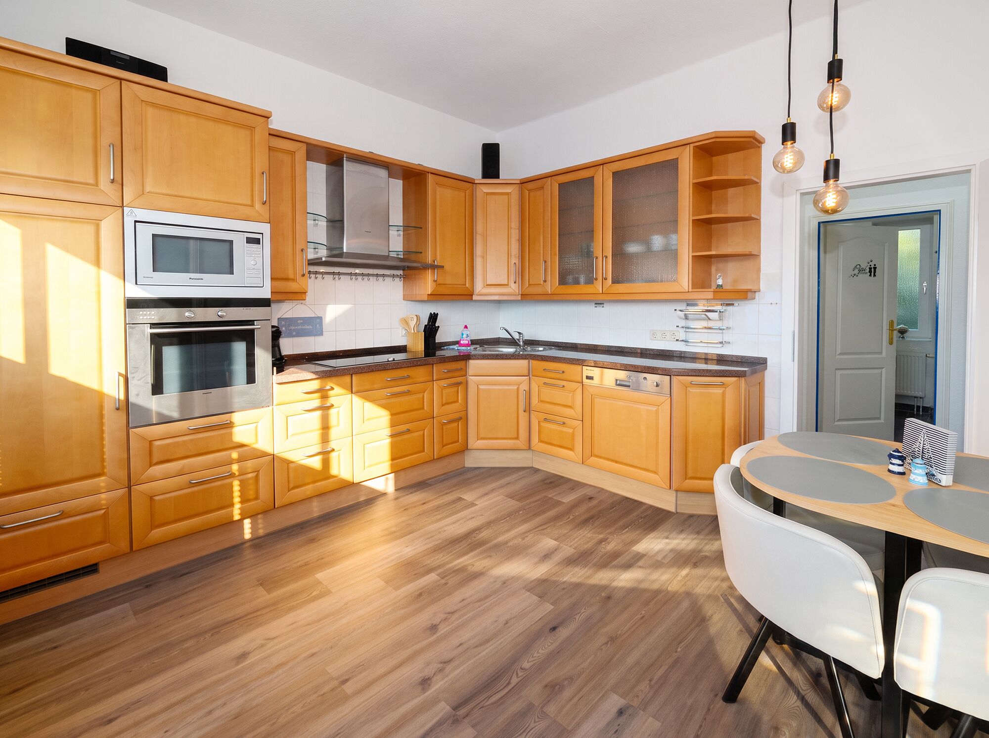 A modern kitchen with wooden cabinets, stainless steel appliances, and a dining area with a round table.