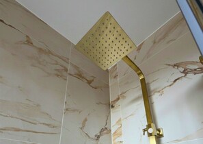 A shower with a square, perforated head and a curved gold fixture.